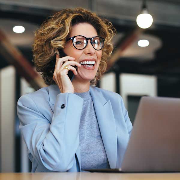 woman on phone with laptop open, smiling and talking