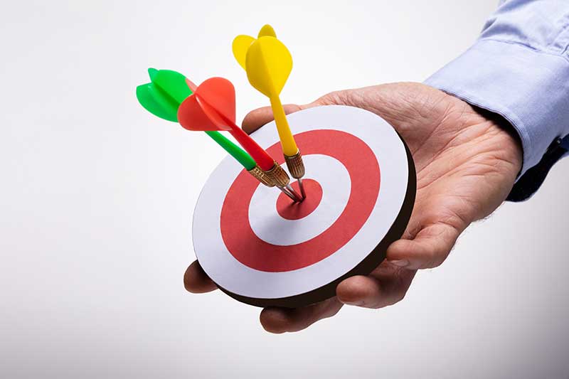 retargeting ads - image of man's hand holding a dartboard target with three darts on the center target