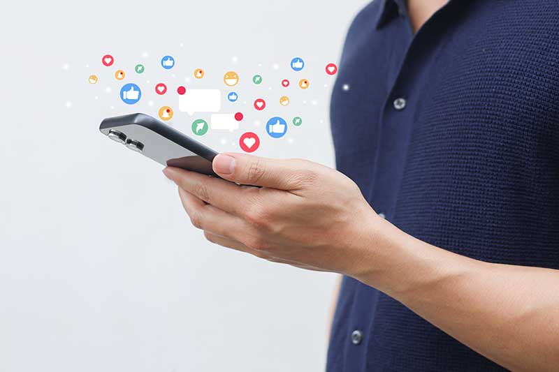 social media advertising services - closeup of man holding cell phone with social media icons and notifications streaming out fancifully